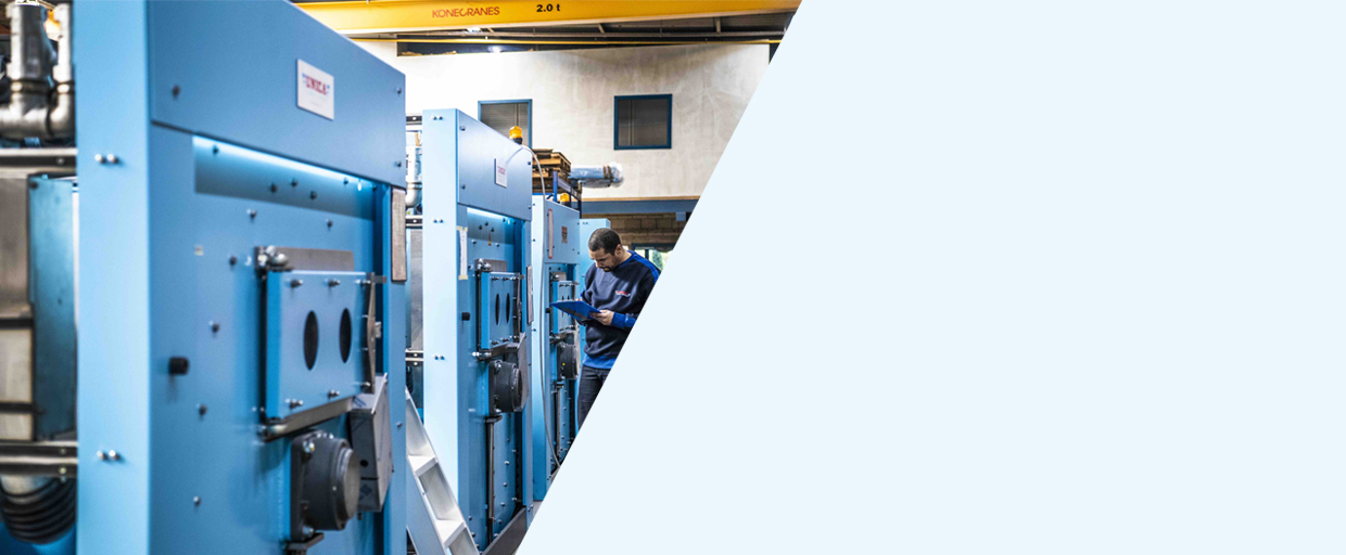 Row of Unica washer-extractors on the assembly floor in Merchtem, with an employee checking one of them